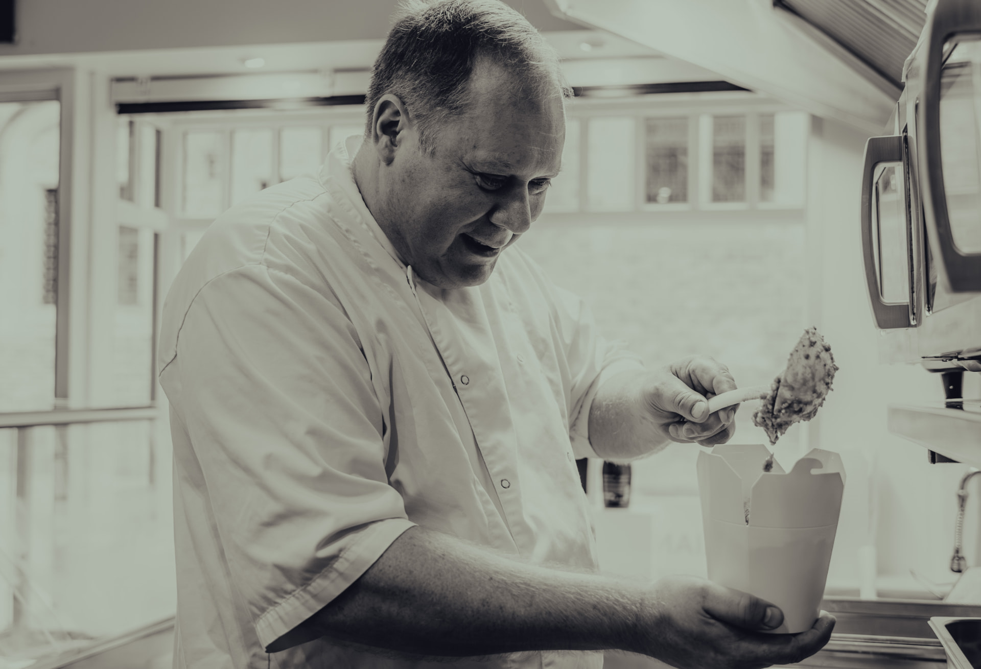 Zwart-witfoto van de chef die verse pasta in een meeneembeker schept